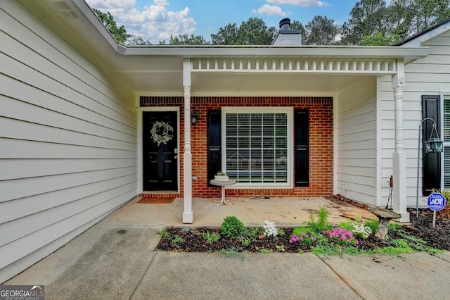 entrance to property with a chimney, a porch, and brick siding
