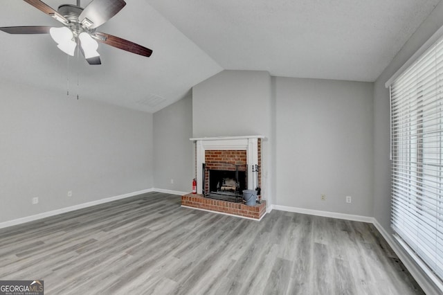 unfurnished living room featuring a healthy amount of sunlight, ceiling fan, a brick fireplace, and wood finished floors