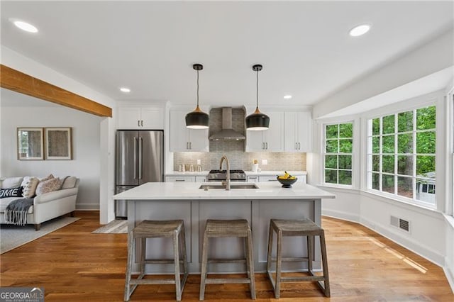 kitchen with visible vents, wall chimney exhaust hood, light countertops, freestanding refrigerator, and white cabinetry