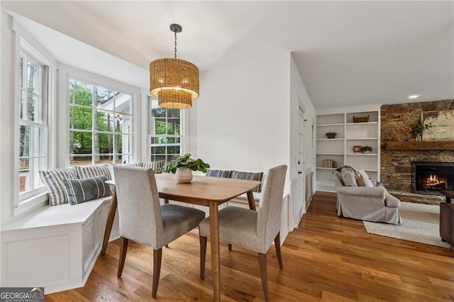 dining space featuring built in features, light wood finished floors, a notable chandelier, and a fireplace