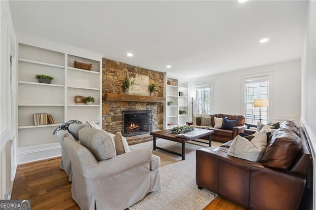 living area featuring built in features, a stone fireplace, and wood finished floors