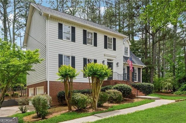 colonial home featuring concrete driveway, an attached garage, and a front yard