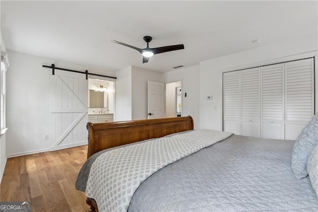 bedroom featuring a closet, wood finished floors, baseboards, ceiling fan, and a barn door