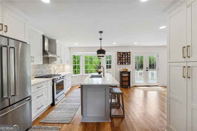 kitchen featuring wall chimney range hood, high end appliances, light countertops, a sink, and dark wood-type flooring