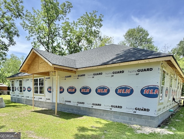 view of side of home featuring roof with shingles and a yard