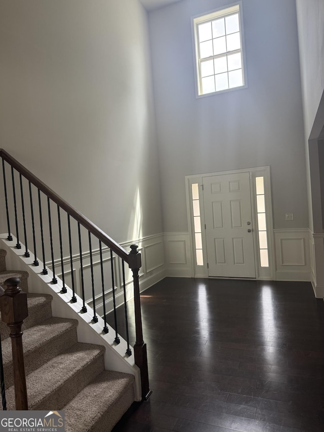 foyer with a decorative wall, a high ceiling, wainscoting, and stairs