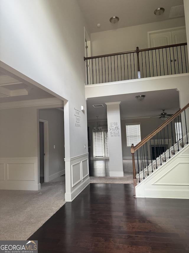 unfurnished living room with crown molding, a wainscoted wall, stairs, a ceiling fan, and wood finished floors