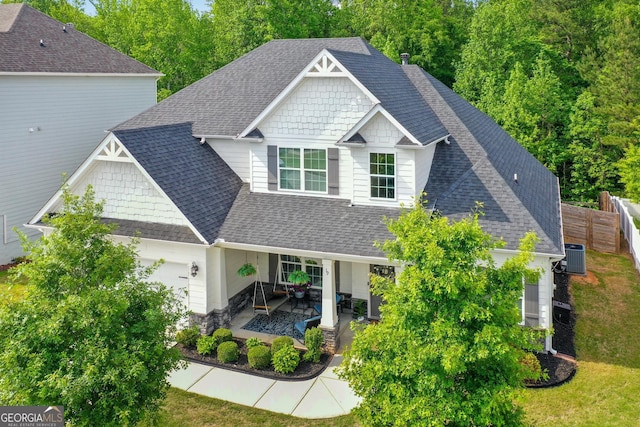 craftsman-style home featuring fence, an attached garage, roof with shingles, and stone siding