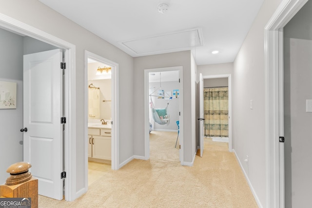 hall featuring baseboards, light colored carpet, a sink, and attic access
