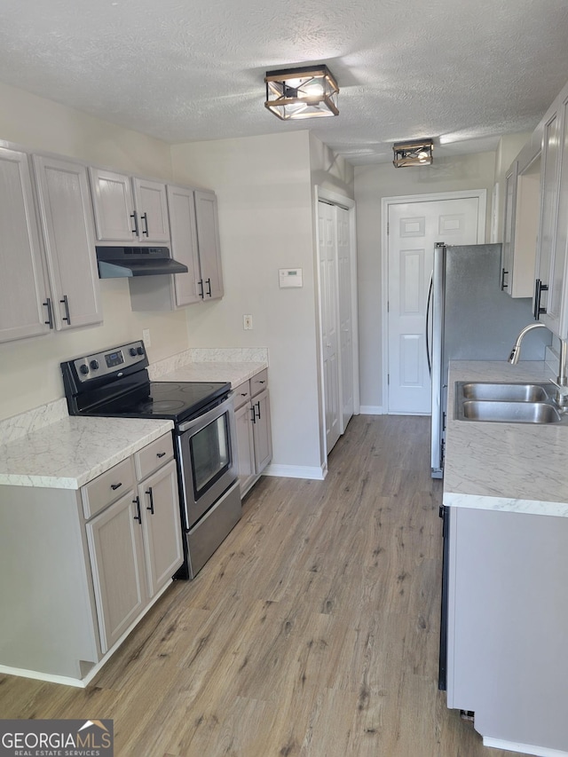 kitchen featuring a sink, light wood-style floors, stainless steel range with electric stovetop, a textured ceiling, and under cabinet range hood