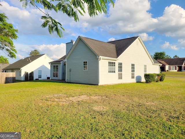 back of house with fence, a yard, and a chimney