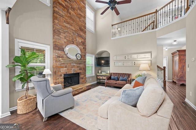 living room featuring a high ceiling, plenty of natural light, a ceiling fan, a fireplace, and baseboards