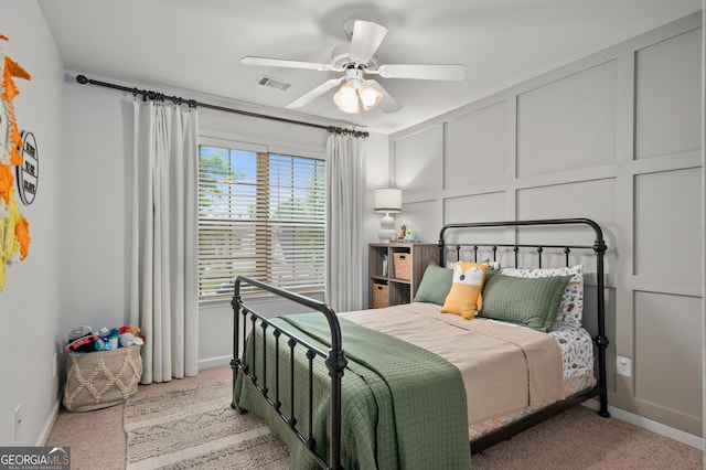 carpeted bedroom featuring ceiling fan, a decorative wall, baseboards, and visible vents