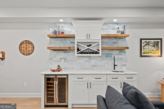 bar featuring wine cooler, light wood-style flooring, a sink, indoor wet bar, and backsplash
