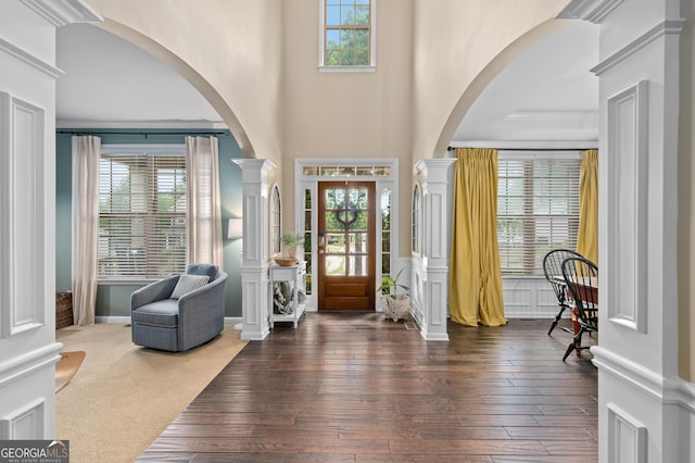 foyer with dark wood-type flooring, a towering ceiling, ornate columns, and arched walkways