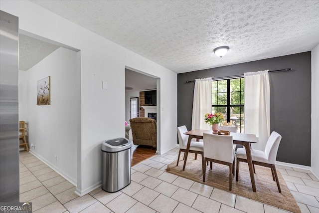 dining room featuring baseboards, a textured ceiling, light tile patterned floors, and a fireplace