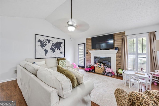 living area featuring a ceiling fan, wood finished floors, baseboards, lofted ceiling, and a glass covered fireplace