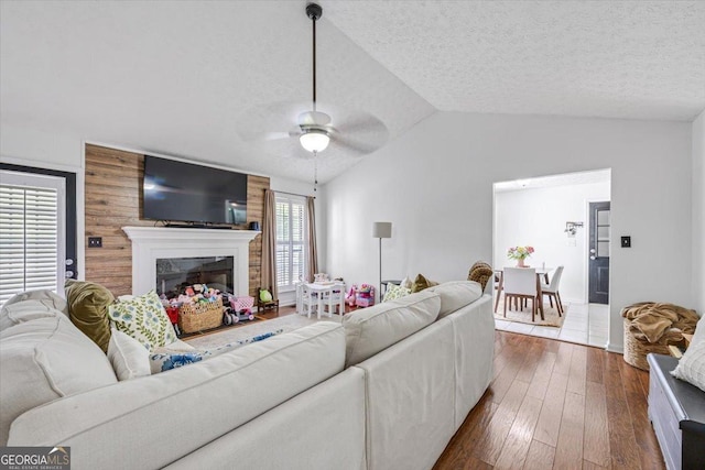 living room featuring a fireplace, a textured ceiling, a ceiling fan, lofted ceiling, and dark wood-type flooring