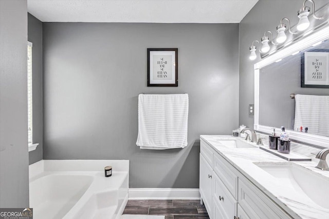 full bath featuring a garden tub, a sink, baseboards, and wood finished floors