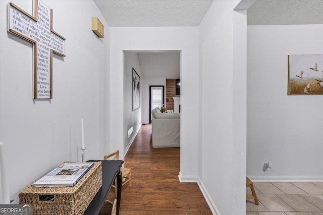 hallway featuring baseboards, wood finished floors, a textured ceiling, and visible vents