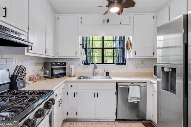 kitchen with a sink, light countertops, stainless steel appliances, a ceiling fan, and under cabinet range hood