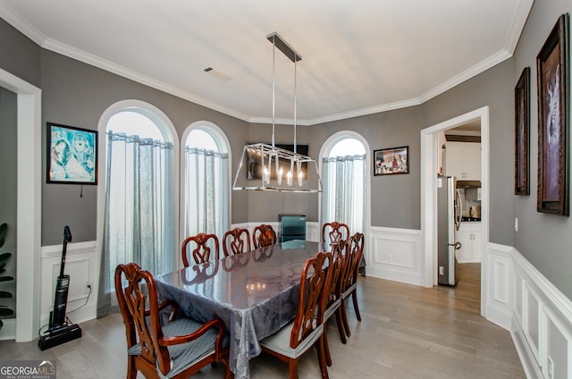 dining space with visible vents, crown molding, wainscoting, a decorative wall, and light wood-style floors