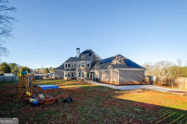 rear view of house with a lawn, roof mounted solar panels, a chimney, and a fenced backyard
