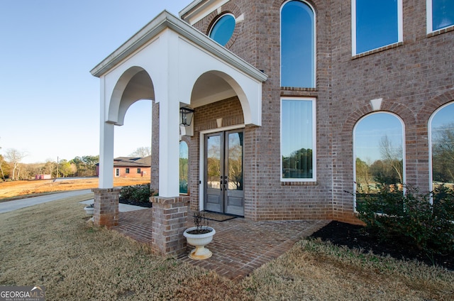 doorway to property featuring brick siding, a yard, and french doors