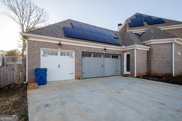 exterior space featuring driveway, roof with shingles, brick siding, roof mounted solar panels, and an attached garage
