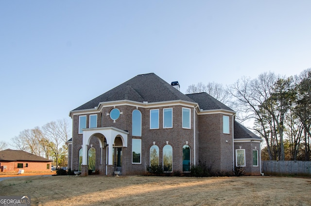french provincial home featuring fence, a chimney, a shingled roof, and brick siding