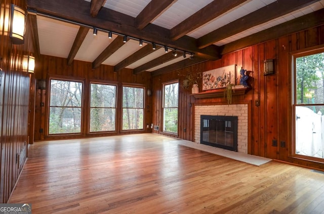 unfurnished living room with track lighting, wood finished floors, a wealth of natural light, and beamed ceiling