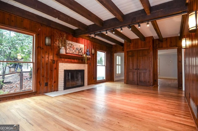unfurnished living room with rail lighting, wood walls, beam ceiling, and wood finished floors