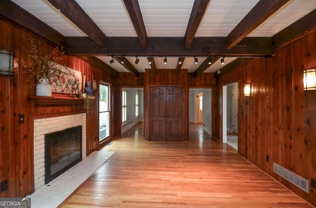 unfurnished living room featuring wooden walls, rail lighting, wood finished floors, beamed ceiling, and visible vents