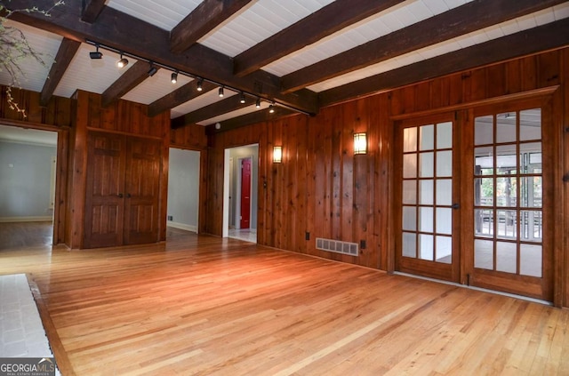 unfurnished living room with track lighting, wood-type flooring, wood walls, beamed ceiling, and visible vents