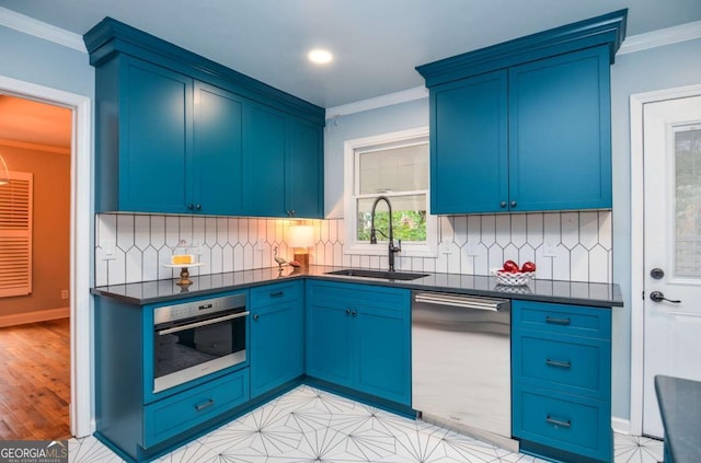 kitchen featuring blue cabinetry, crown molding, appliances with stainless steel finishes, dark countertops, and a sink