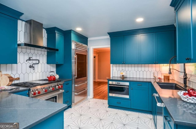 kitchen with high end appliances, dark countertops, wall chimney range hood, tasteful backsplash, and a sink