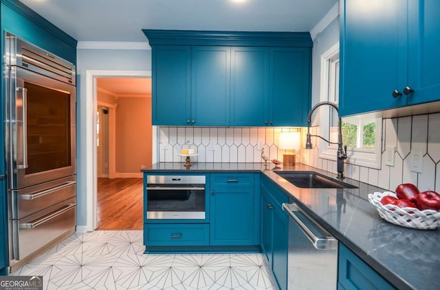 kitchen featuring crown molding, blue cabinets, tasteful backsplash, a sink, and stainless steel appliances