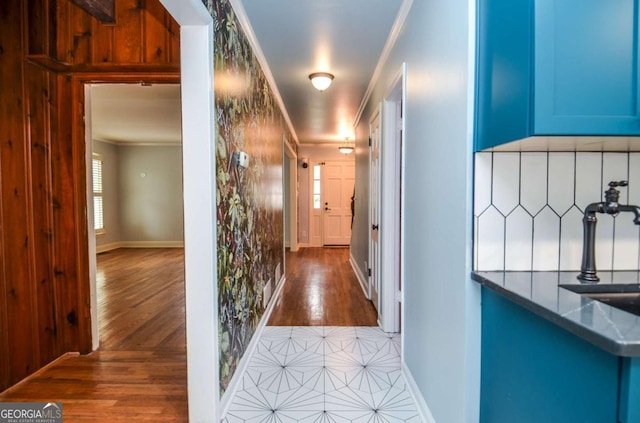 corridor with crown molding, baseboards, wood finished floors, and a sink