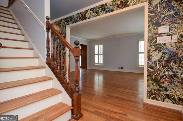 staircase with visible vents, wood finished floors, baseboards, ornamental molding, and wallpapered walls