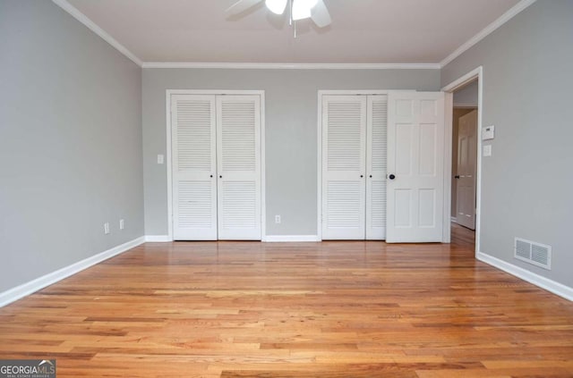unfurnished bedroom with crown molding, multiple closets, light wood-type flooring, and visible vents