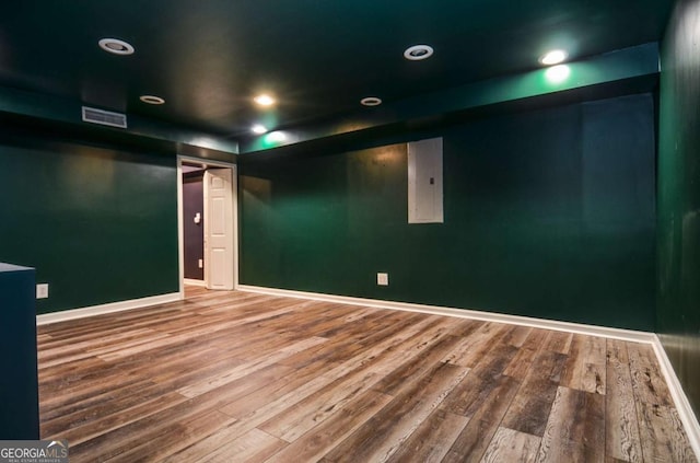 empty room with electric panel, visible vents, wood finished floors, baseboards, and recessed lighting