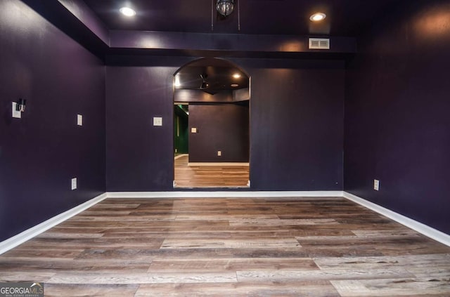 empty room with arched walkways, baseboards, visible vents, and wood finished floors