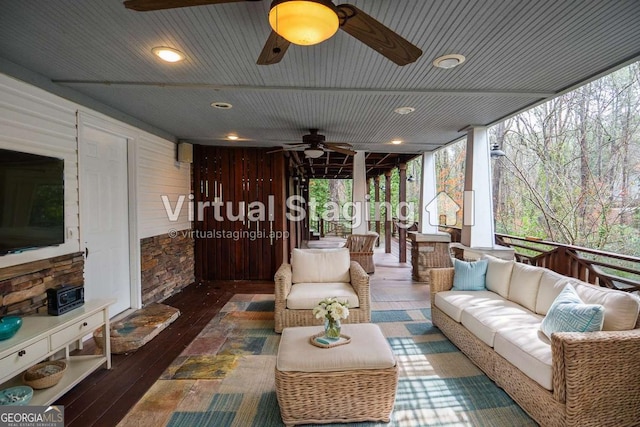 sunroom / solarium with a wall of windows, hardwood / wood-style flooring, a ceiling fan, and an outdoor hangout area