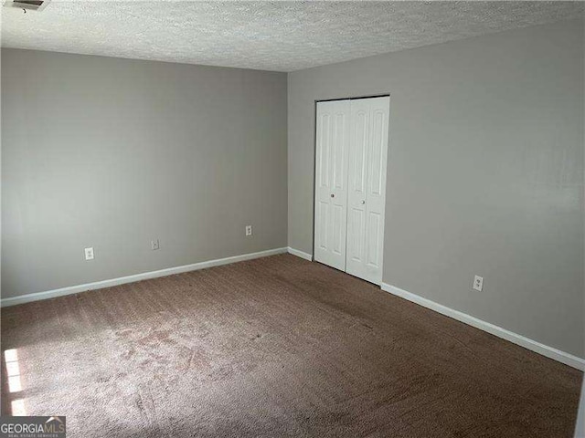 unfurnished bedroom featuring baseboards, a closet, dark colored carpet, and a textured ceiling