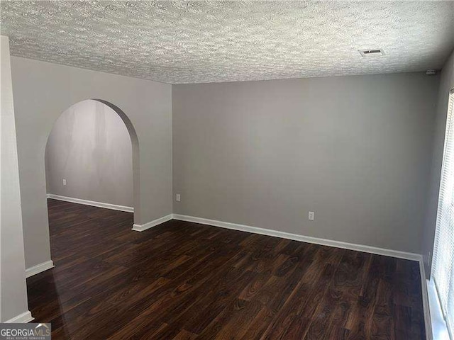 unfurnished room with a textured ceiling, arched walkways, and dark wood-style floors