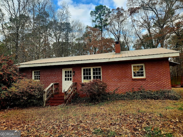 back of property featuring brick siding, a chimney, and metal roof