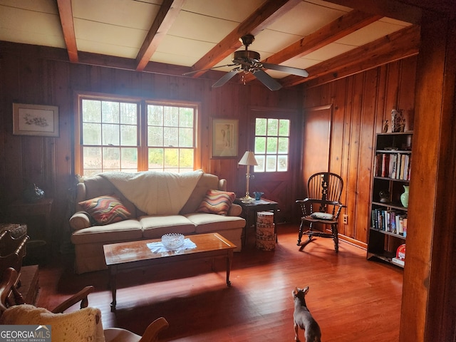 living room with beamed ceiling, a ceiling fan, wood walls, and wood finished floors