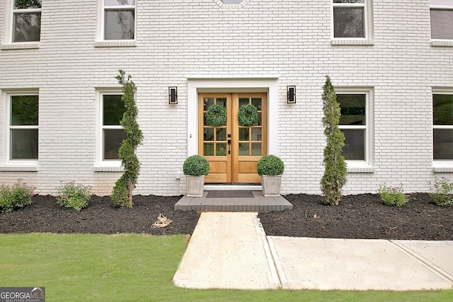 entrance to property with a yard, brick siding, and french doors