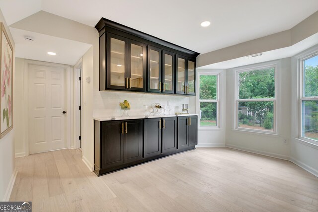bar featuring light wood-type flooring, decorative backsplash, wet bar, and baseboards