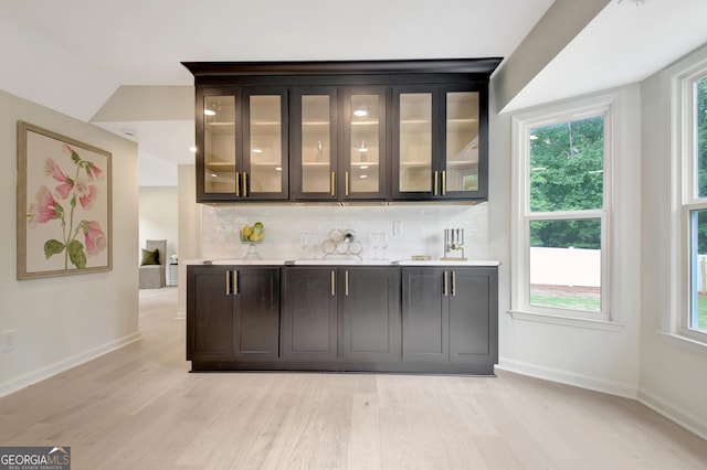 bar featuring baseboards, light wood-style flooring, lofted ceiling, and backsplash